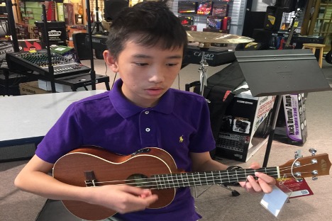 Kid in purple shirt playing ukulele at a musical store