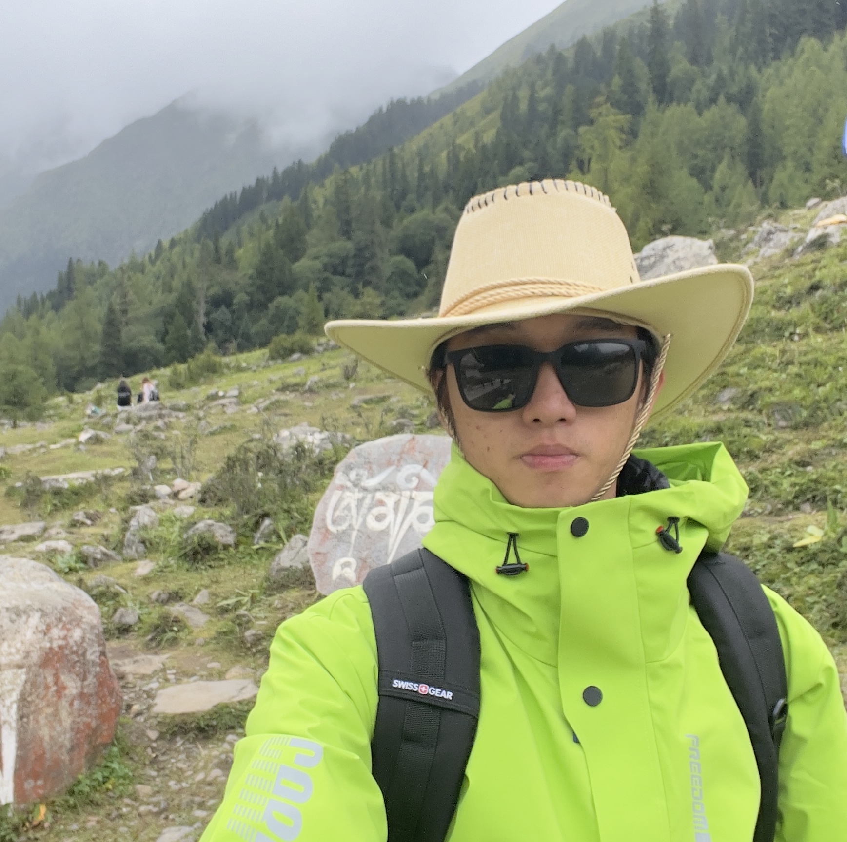 boy wearing white cowboy hat and neon raincoat under a mountain